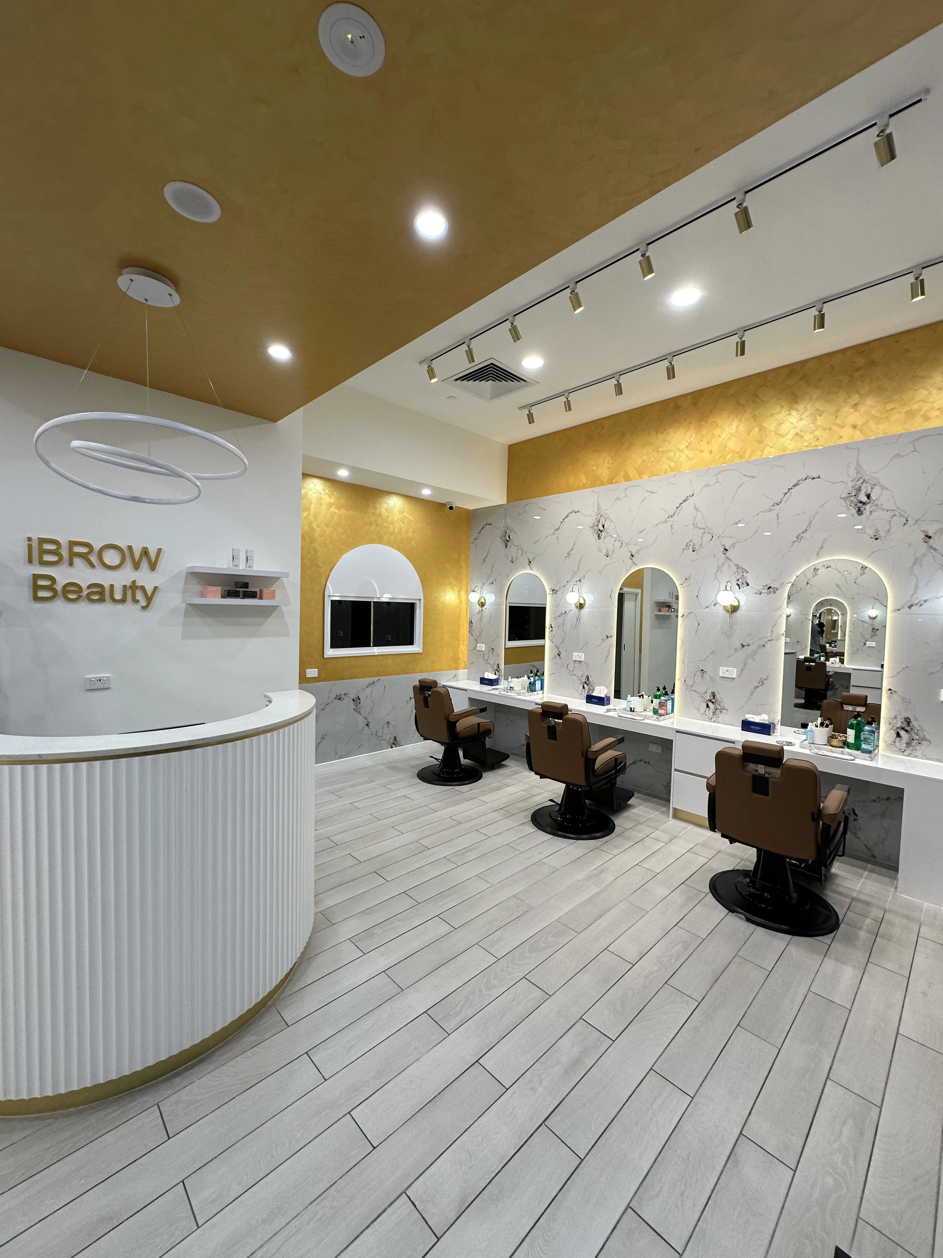 Full salon interior — reception, tan leather chairs and marble stations under the gold ceiling