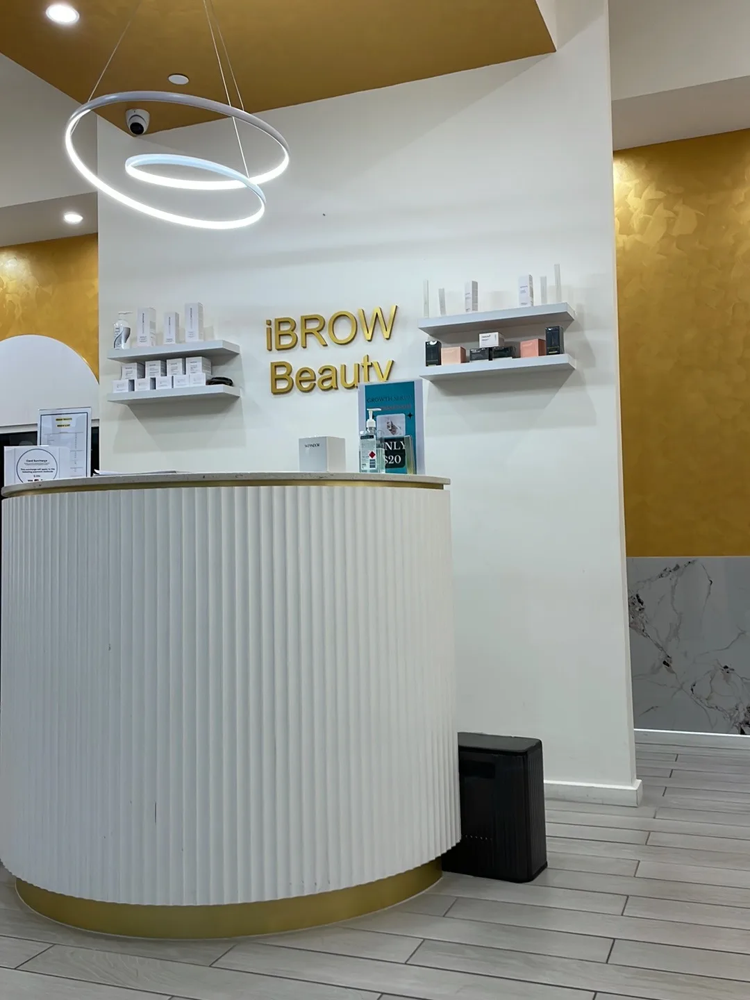 Reception counter close-up — gold iBROW Beauty sign, retail shelves and the branded desk
