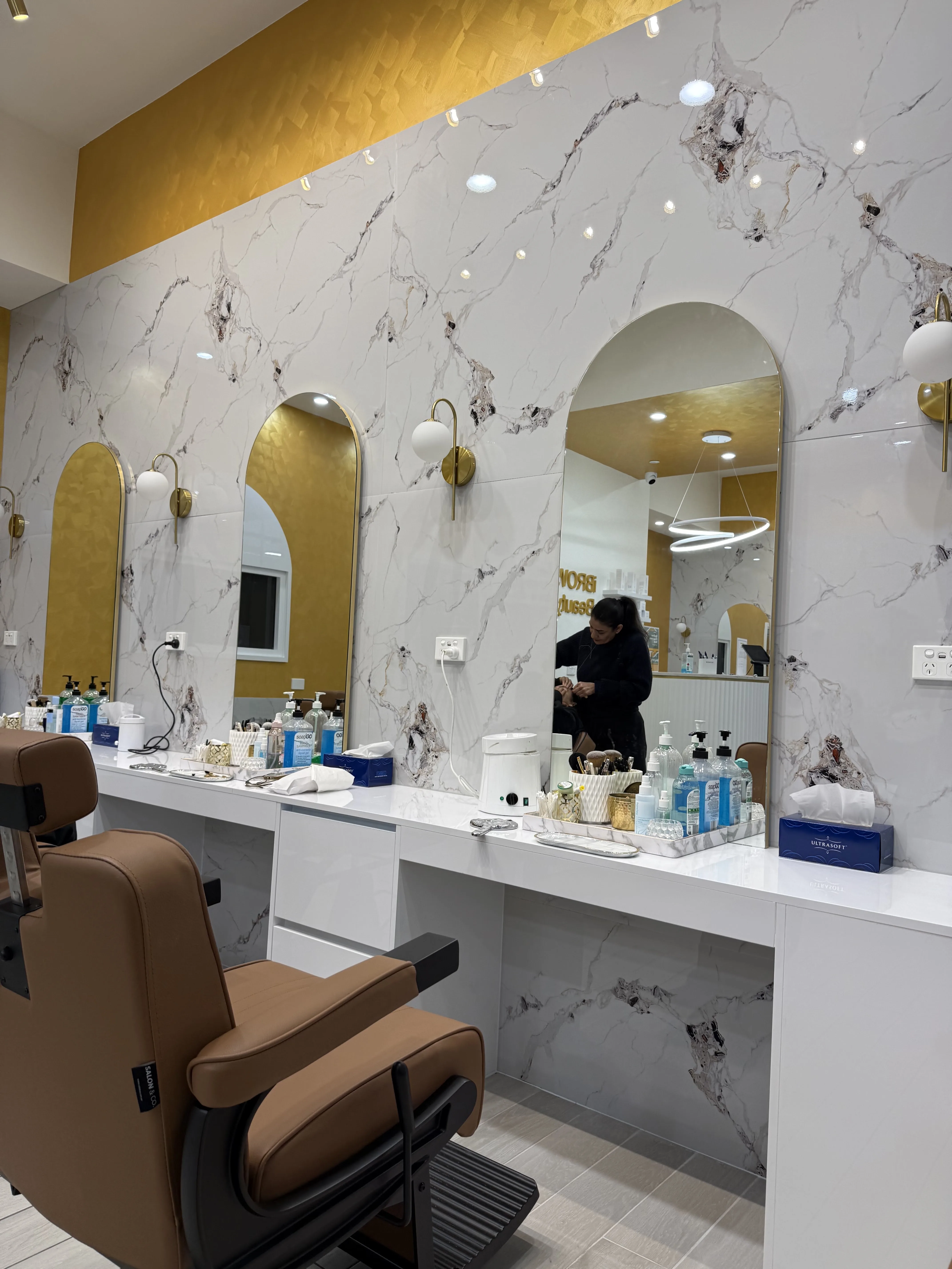 Row of marble styling stations with arched mirror niches and gold sconces